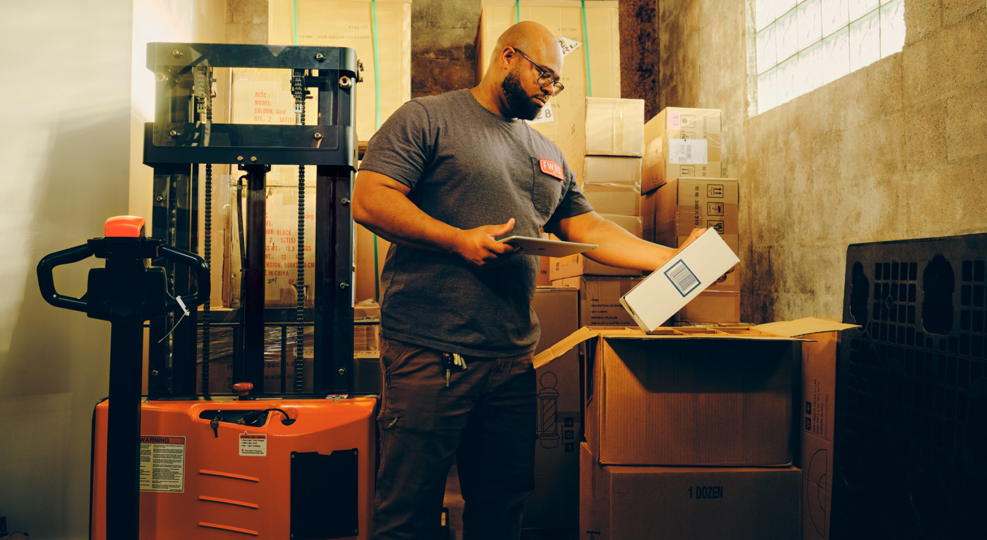 A person in a warehouse holds a box with their left hand and an iPad with their right hand while taking inventory on the device. A diagram to the right of the image shows the features of the 金刚电竞官方入口网址 Inventory platform.